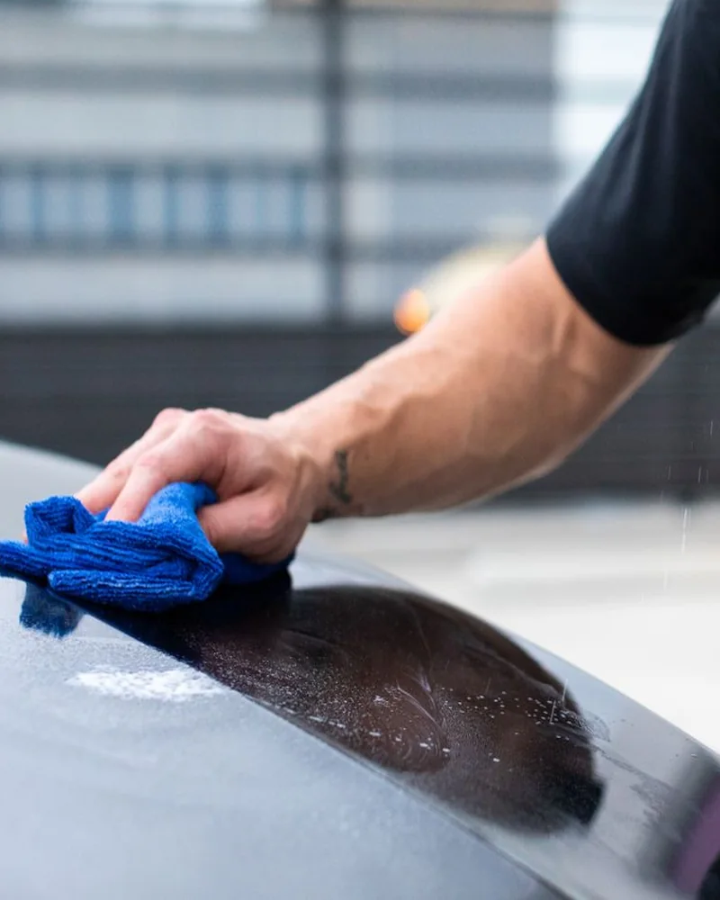 Main qui essuie un capot sombre avec une microfibre bleue